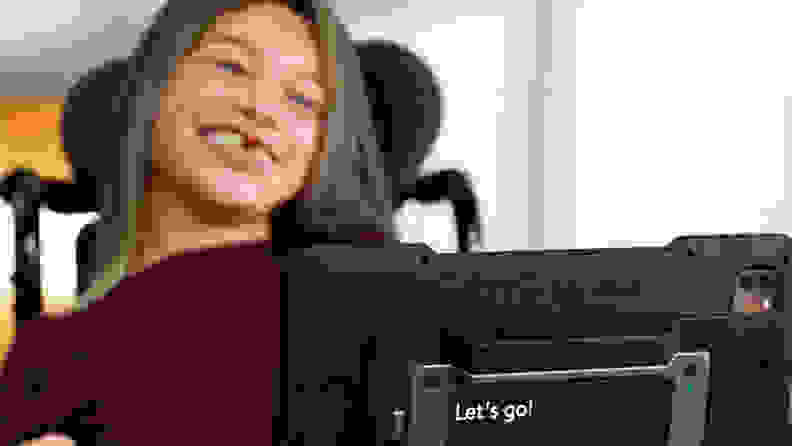 A little girl in a wheelchair looking at an AAC device.
