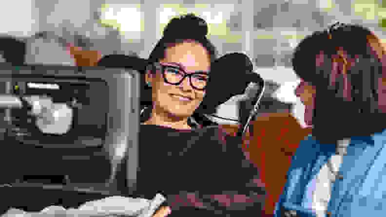 A woman in a wheelchair using an AAC device while conversing with another woman