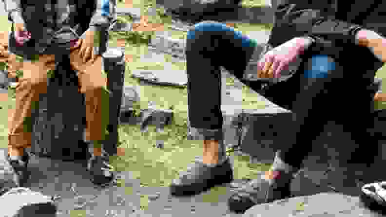 A child and a man sitting together, each wearing a pair of Acorn Moc Slippers in men's sizes.