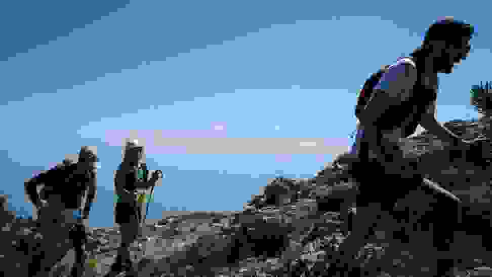 A group of three hiking together in the mountains, blue sky stretching out behind them