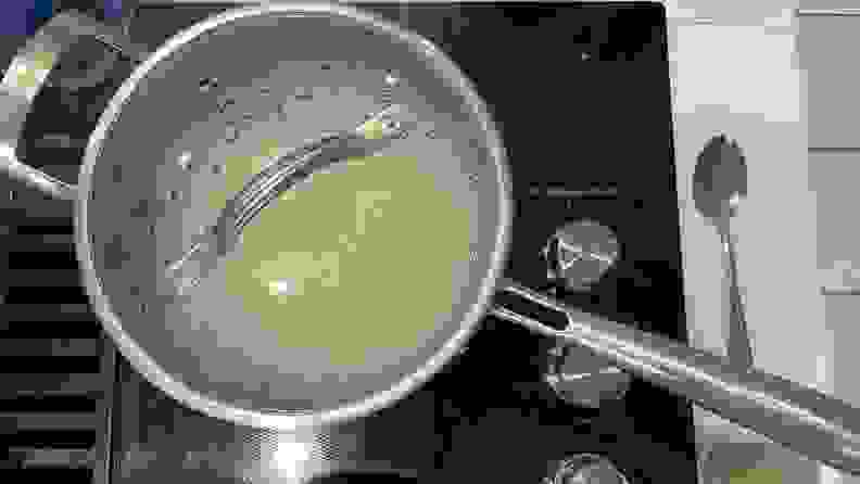 A Guy Fieri Flavortown Laser Titanium pot with lid attached boiling on top of cooktop.