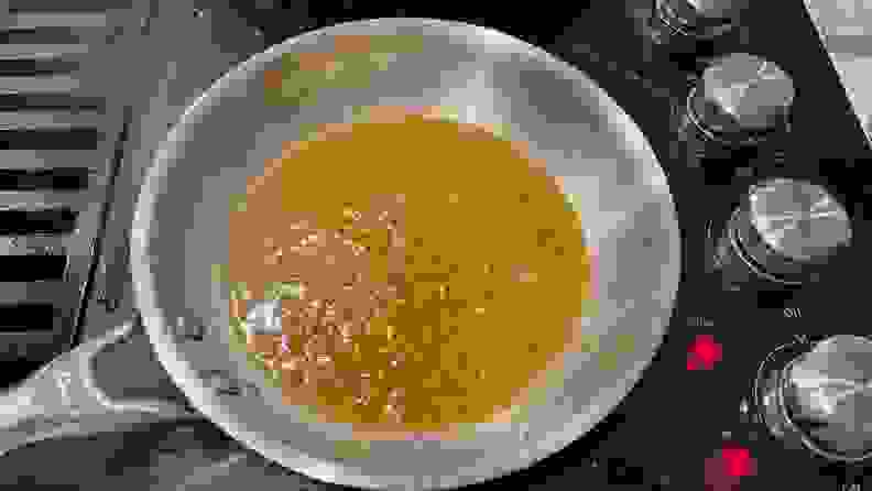 Leftover fond inside a stainless steel pan on a black stovetop.