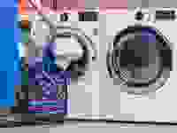 Woman loading a white towel into the white LG WM3700HWA front-loading washing machine, which is sitting next to a matching front-loading dryer.