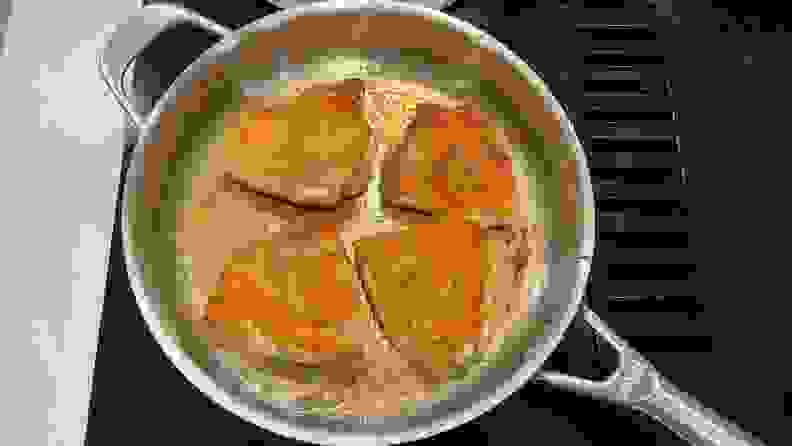 Four piece of meat being cooked in a stainless steel pan on a black stovetop.