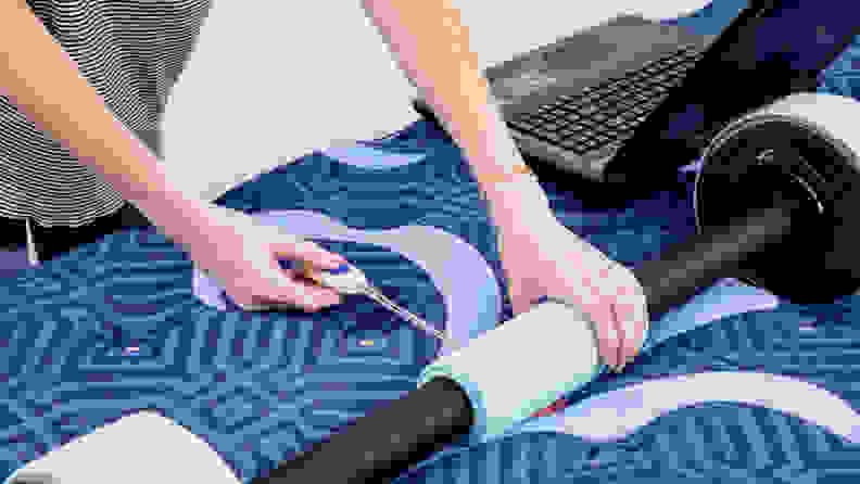 A person measuring the pressure underneath a barbell resting on a mattress.