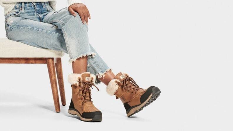 Pair of Ugg Adirondack boots worn on woman's feet with cat looking from the inside of a house. Pair of Ugg Adirondack boots sitting upright.