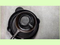 A pile of cast-iron skillets on a light grey surface.