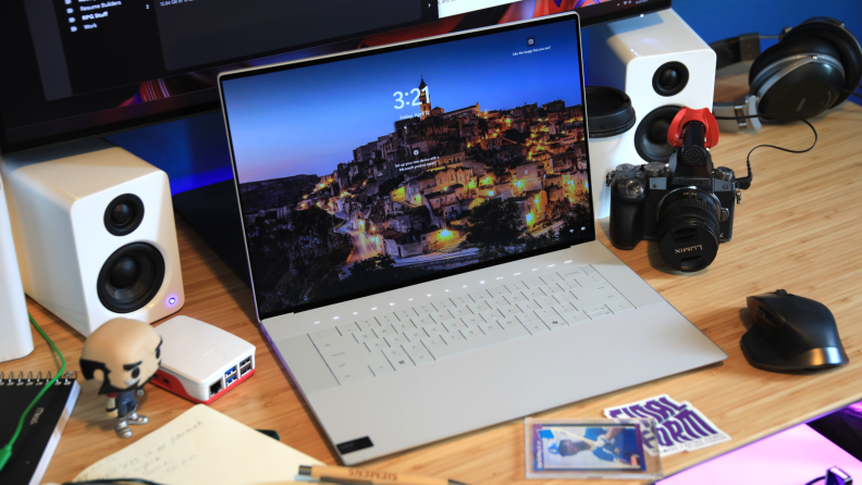 The Dell XPS 16 laptop on a desk next to two white speakers and desk supplies.