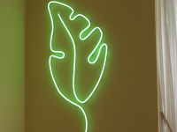 Green leaf-shaped neon light mounted on wall inside of home next to curtained window.