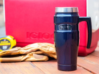 A Thermos travel mug sitting on a table next to a cooler.
